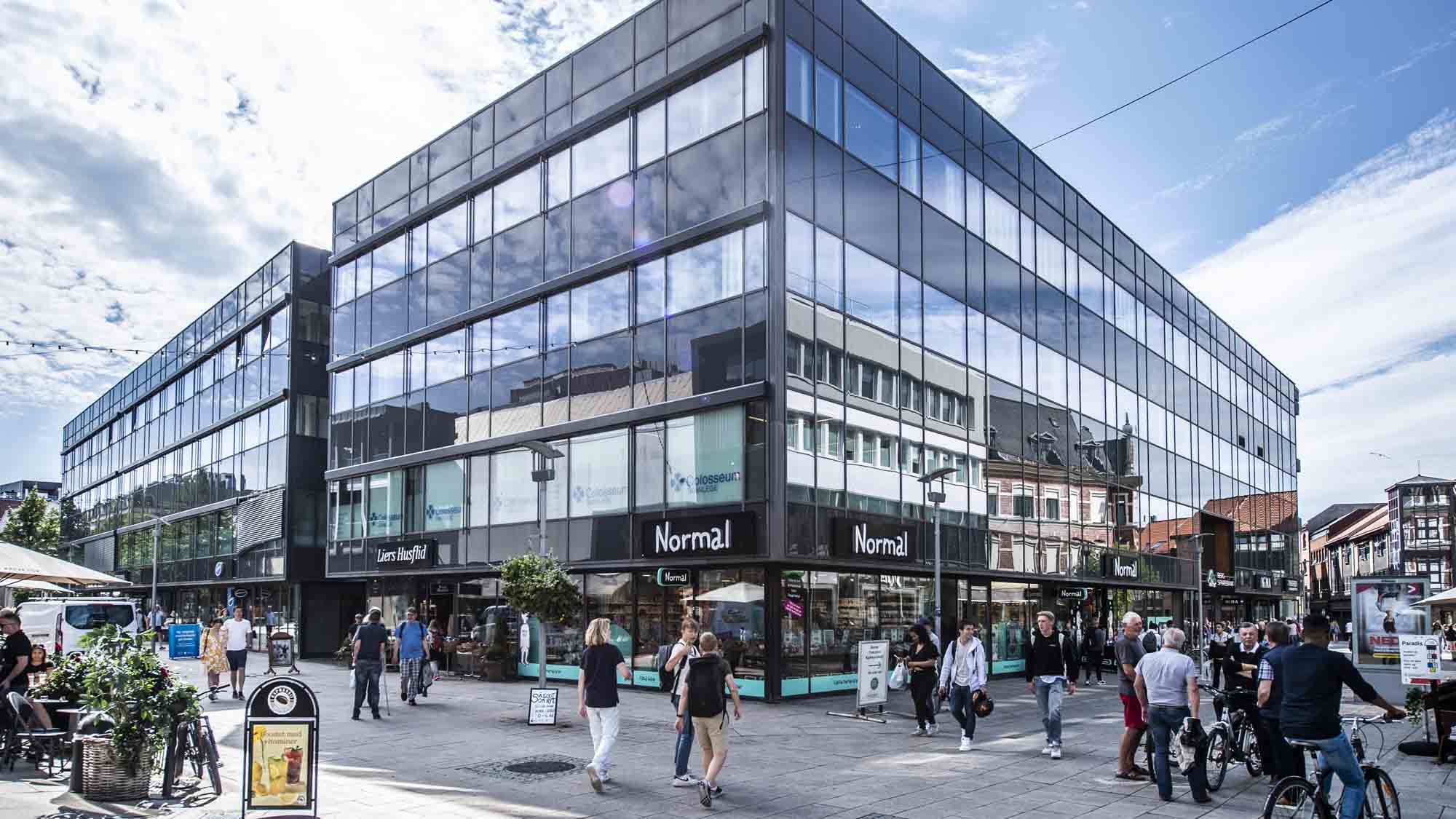 Mot blå himmel en bygård over tre etasjer midt i gågaten i Fredrikstad med yrende folkeliv rundt