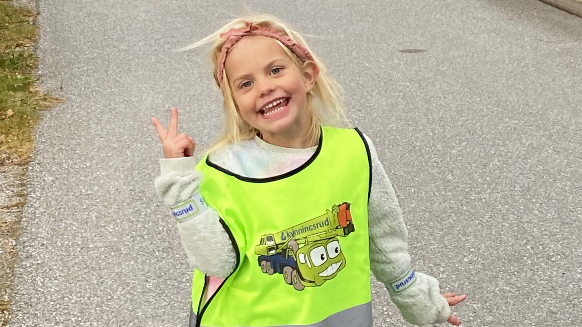 Young smiling girl wearing reflective vest with a green mobile crane on it