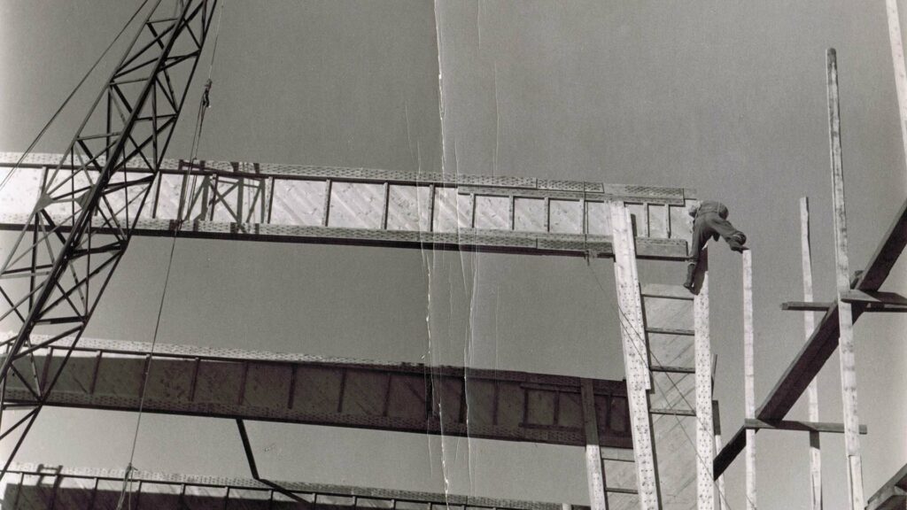 svart-hvitt bilde av byggeprosjekt på 50-60-tallet. Mann balanserer på toppen.