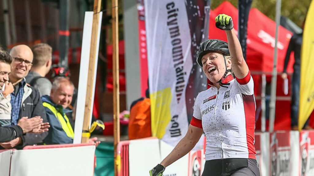 Norgesmester terreng Ingrid sykler i mål og markerer seieren ved å strekke en hånd i været mens hun jubler